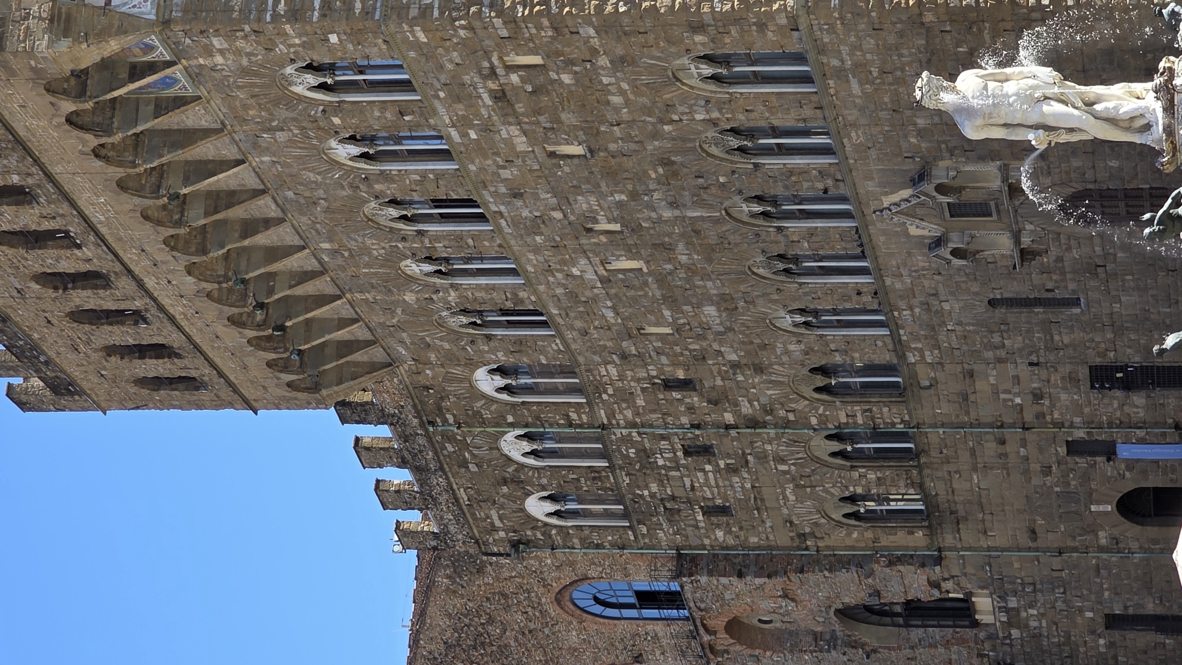 The rusticated wall and blue-shuttered windows of the Palazzo Vecchio above a marble statue
