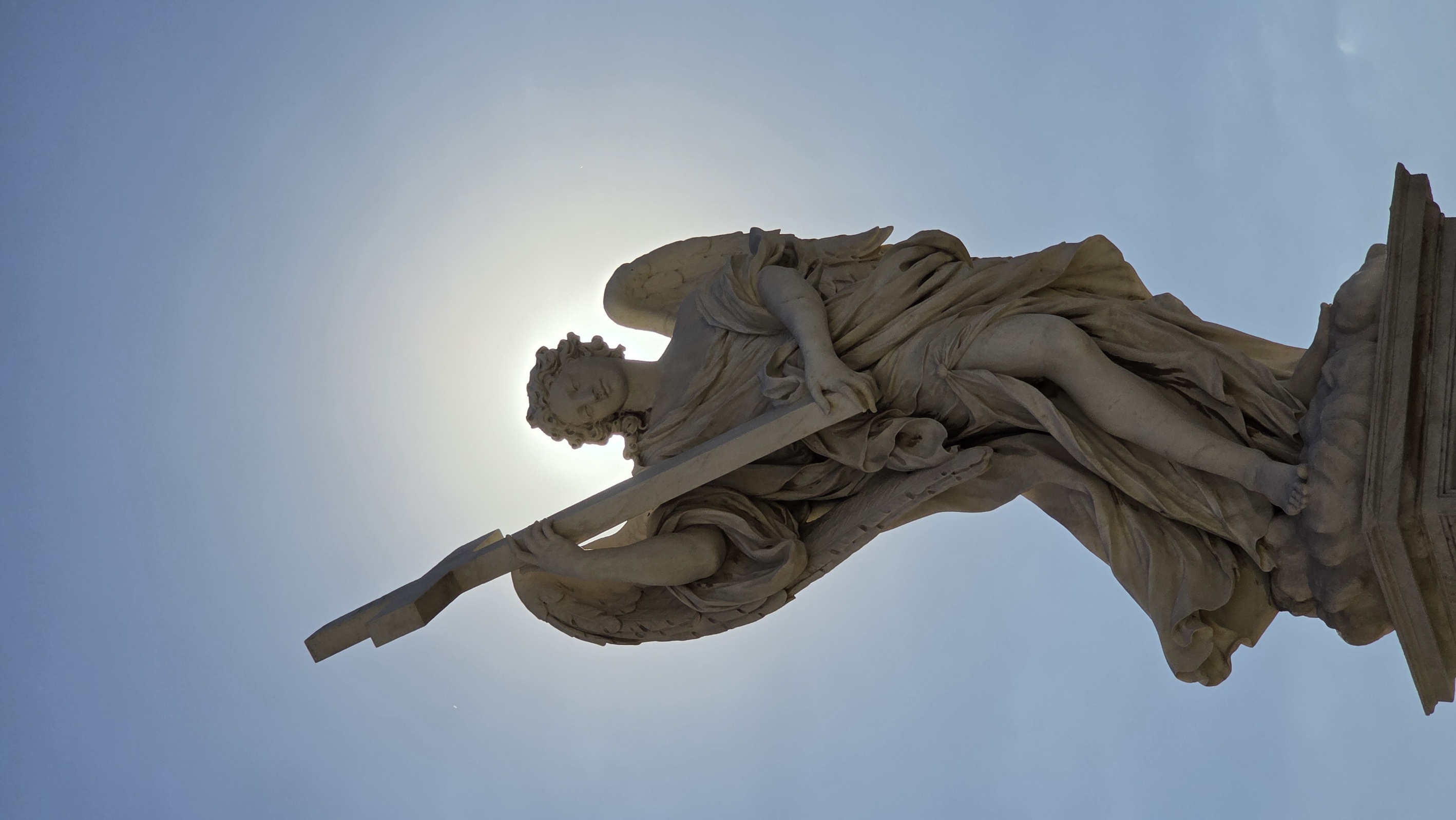 A bridge angel holding a cross, backlit by the sun