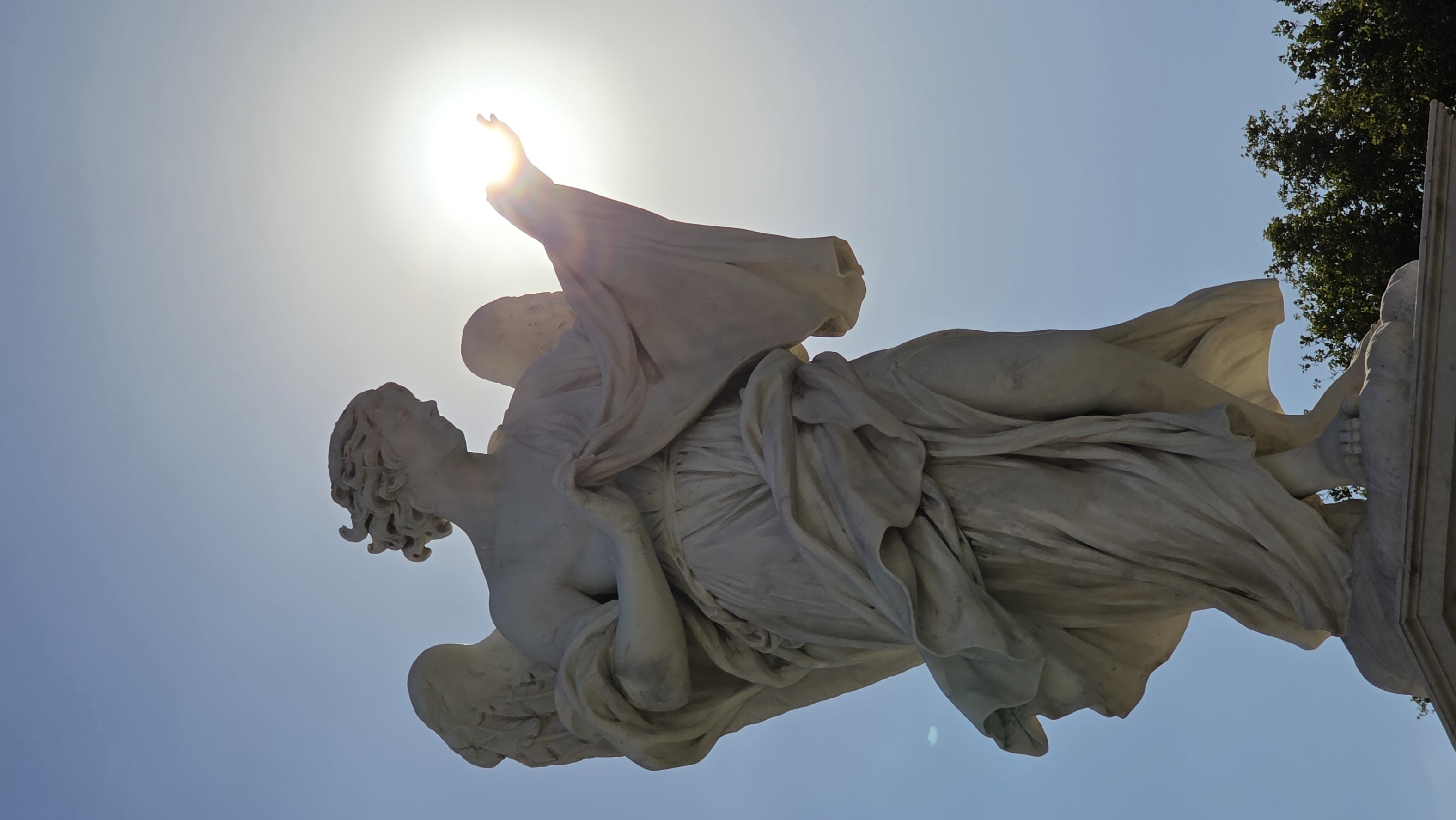 An angel statue on the bridge with the sun blazing behind it