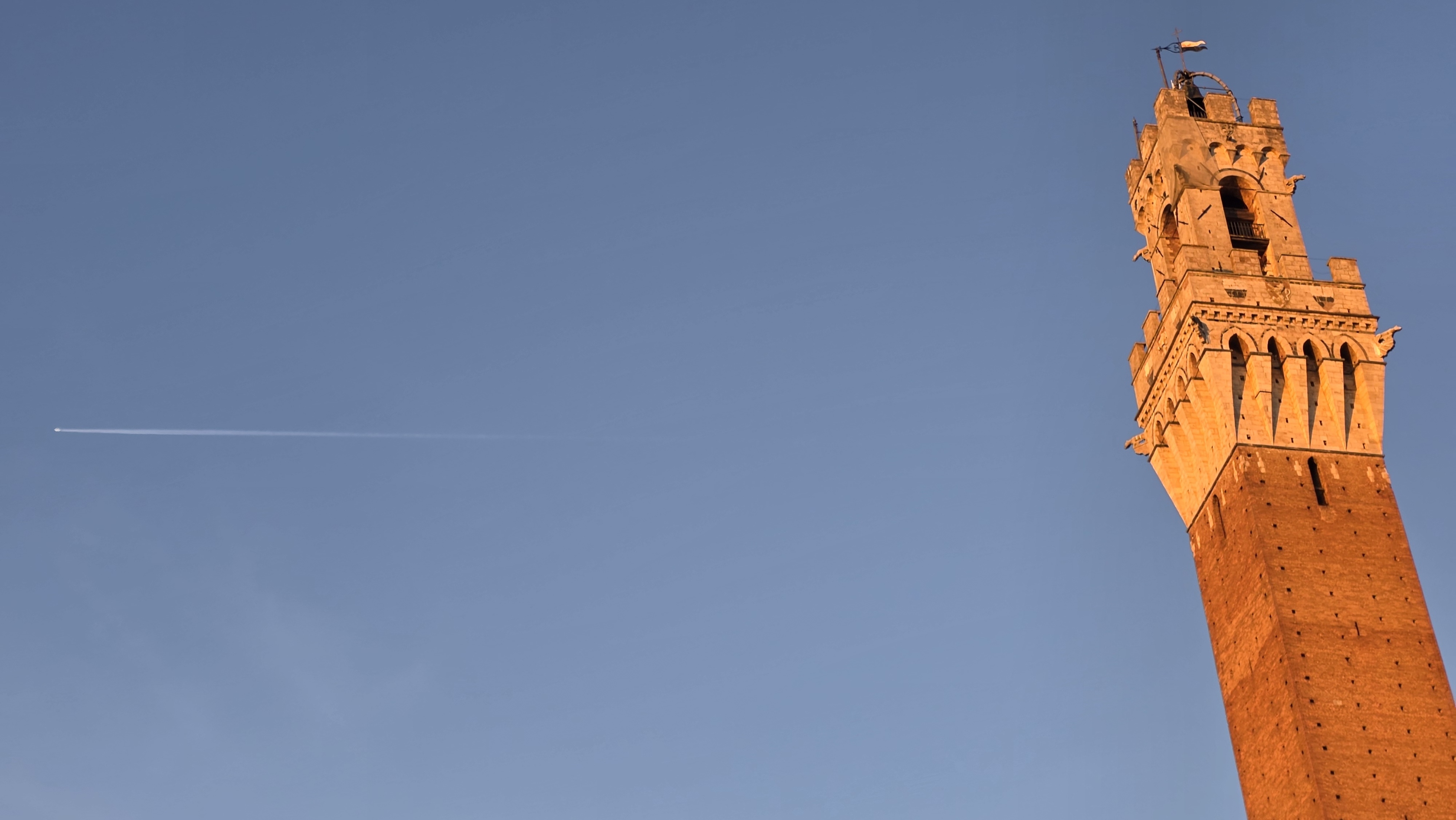 The tip of the Torre del Mangia alone in a vast pale sky