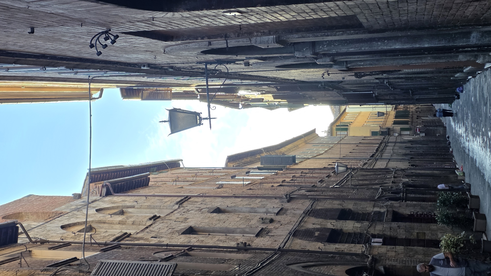 A steep narrow street in morning shadow with a lamp and a strip of blue sky