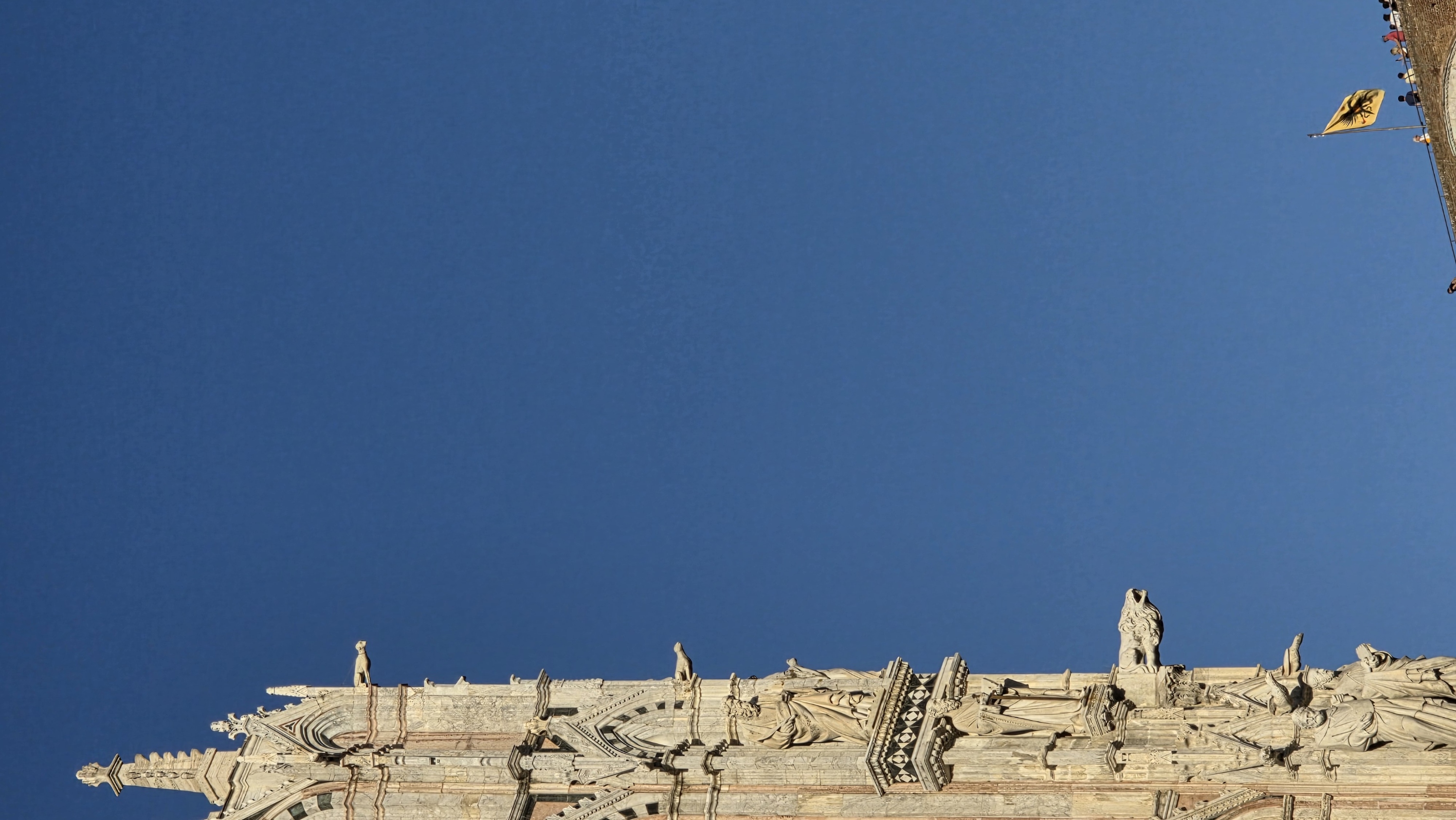 A slender cathedral pinnacle with a gargoyle against blue