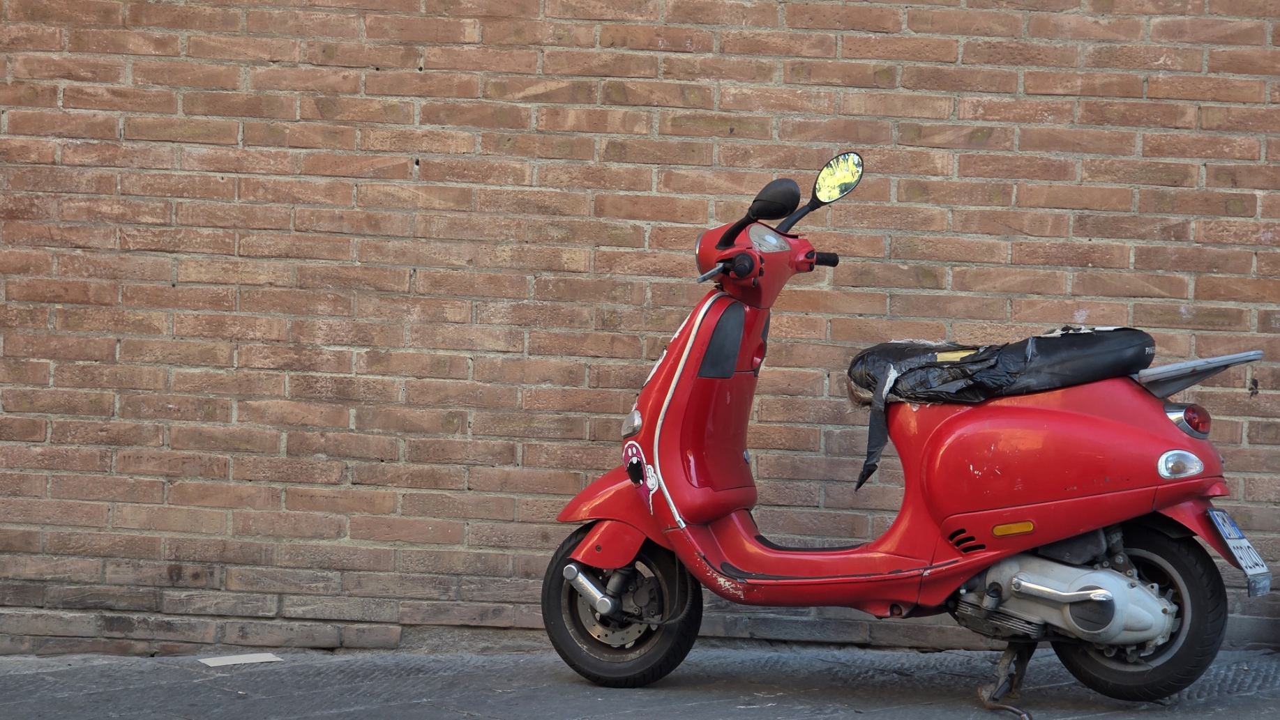 A red scooter parked against a bare brick wall